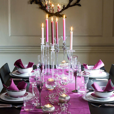 Déco table Noël couleur noir et rose fushia. Sur la table noire chemin de table en coton rose fushia, bougeoirs en verre et argent