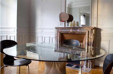 Peinture gris perle pour la déco d'une salle à manger qui mélange les styles avec une cheminée en marbre marron une table en verre mderne et des chaises de styles scandinaves noires