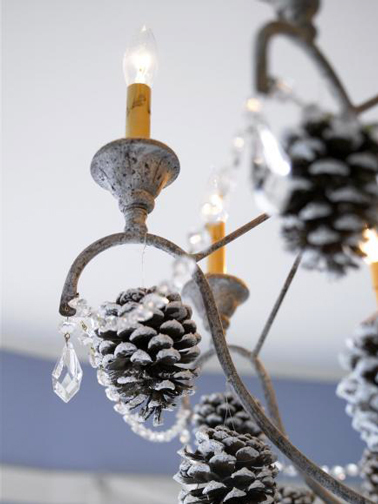 Décoration de Noël sur le lustre de la salle à manger réalisée avec des pommes de pin bombées de neige artificielle suspendues sous chaque lampe bougies