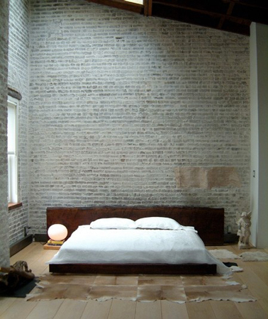 Déco chambre zen avec mur en pierre de parement gris et grand lit sur estrade. La tête de lit en bois foncé apporte un note confortable et chaleureuse.