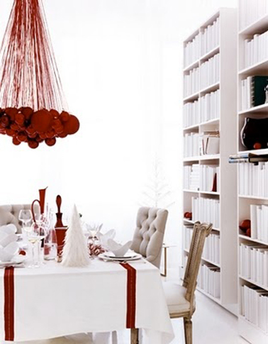 Déco table de Noël en rouge et blanc : Sur la nappe blanche deux larges rubans rouge, bougeoirs rouge et suspension réalisée avec une accumulation de boules rouges suspendues au plafond avec cordon rouge