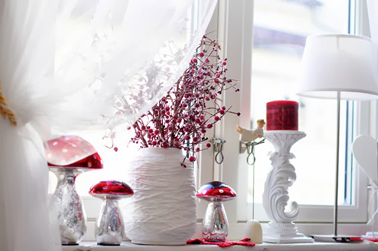 Une composition de vase et bougeoir blanc avec bouquet et bougie parfumée rouge pour un Noël scandinave