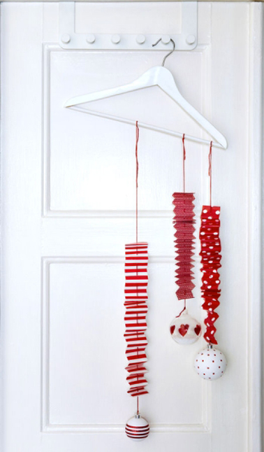 Une décoration de porte pour Noël originale en rouge et blanc réalisée avec des guirlandes de papier et des boules accrochées à un simple porte-manteau