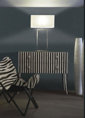 Pour renforcer le style baroque d’un salon et créer un point lumineux et ludique, une peinture pailletée noir Studio sur un fond peint en gris anthracite révélée par une lampe posée au centre du mur sur une commode qui ne manque de caractère avec ses rayures noires et blanches.  Peinture Paillett’ Les décoratives.