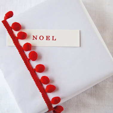 Pour faire des paquets cadeaux de Noël en rouge et blanc, du papier kraft blanc, bordé d'un ruban à pompons rouge et une étiquette imprimée en rouge pour personnaliser avec le prénom ou simplement Noël