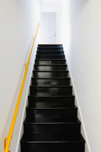 Exemple d'escaliers en bois relookés avec une peinture noir brillant qui a donné l'occasion de repeindre la rampe elle aussi en jaune lumière qui réveille les murs blancs.