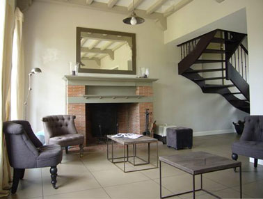 Déco d'un salon d'une maison de campagne où le gris est apporté par le mobilier et le gris anthracite de l'escalier. Peinture murale et double-rideaux couleur écrue