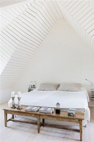 Dans cette chambre aménagée sous les toits, l'architecture du plafond en lambris peint en blanc est l'élément déco mis en avant. Petit clin d'oeil à une ambiance zen, le bouda placé sur la console en bois au pied du lit