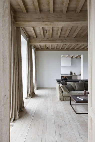 dans ce grand salon aux murs gris perle et au style épuré, la couleur lin des rideaux se cale ton sur ton avec la couleur du plafond plancher. Le sol en parquet chêne blanchi révèle l'aspect chaleureux du coin canapé décliné en dégradé de lin et gris.