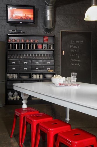 Un style retro chic pour une cuisine rouge et noir avec un vaisselier et des murs briques peints en noir satin noir et des tabourets Tolix rouge autour d'une table bois peinte en blanc laqué