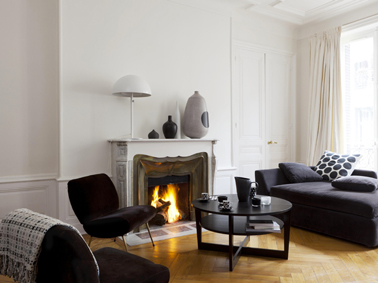 Une peinture lin clair et blanc pour créer une ambiance cocooning dans un salon autour de la cheminée et des fauteuils et canapé noir