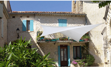 Déco terrasse maison provençale avec une grande voile d'ombrage blanche fixée sur les murs de la maison. Castorama