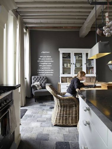Dans une cuisine grise, un mur couleur taupe apporte une note chaleureuse autour du carrelage sol aux nuances de gris et noir et des meubles anciens repeints gris perle. 