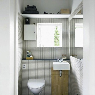 La décoration de petits WC bien pensée pour agrandir l'espace. Les murs sont carrelés de faïence blanche jointée en gris, le haut des murs est exploité pour les rangements et le grand miroir permet de donner une impression de largeur