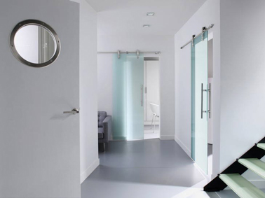 Dans le couloir d’un appartement moderne des Portes en verre trempé coulissantes soulignent le design de l’espace Dans un appartement moderne, la déco du couloir mise sur tous les éléments pour souligner le design de l’espace : peinture des murs d’un blanc immaculé, portes coulissantes en verre trempé et sol en béton peint en gris clair ultra brillant. Coulissant et peinture en vente chez Leroy Merlin