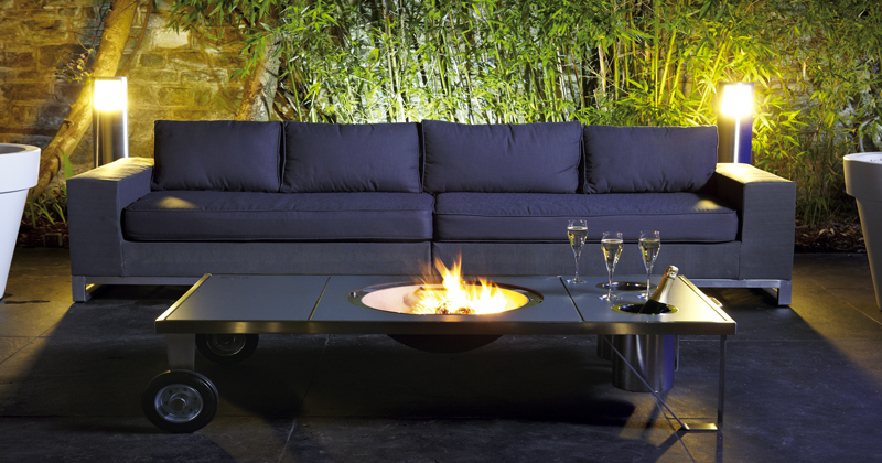 La Table brasero en inox se fait mobilier de jardin design avec son coin cheminée outdoor et ses fonctions de table de jour comme de nuit.
