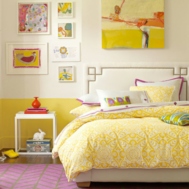 Une peinture couleur jaune Anis en soubassement pour une déco de chambre fille qui a du pep's avec un rappel de jaune avec la housse de couette et les tableaux et dessins crochés au mur au dessus du lit