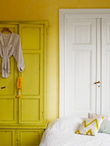 Deux couleurs de jaune pour la peinture d'une chambre : Sur les murs une peinture couleur jaune orangé contraste avec le blanc des boiseries, tandis que l'armoire ancienne est peinte avec un jaune citron lumineux