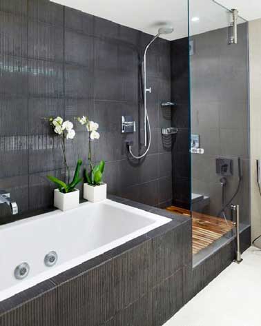 Dans cette salle de bain, l’espace baignoire et douche italienne donne priorité au carrelage gris pour créer l’unité. Le caillebotis en teck compense la dominante grise de l'espace dédié au bain. 