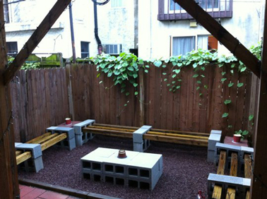 Dans un petit jardin en ville à l'abri des regards derrière les cloisons de bois, des parpaings assemblés en bloc pour faire la table basse, et une association futée de bois et parpaings compose les bancs.