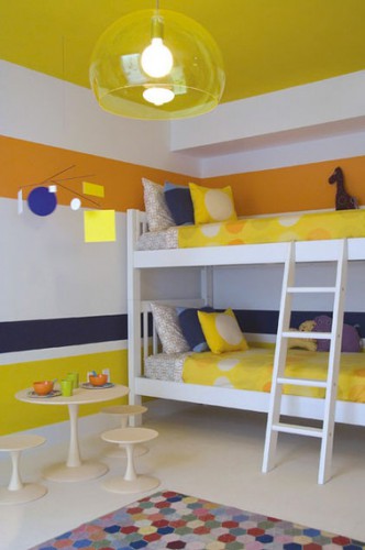 Déco d'une chambre partagée par deux enfants avec des bandes de peinture jaune acidulé, orange et bleu marine sur une base de peinture blanche.