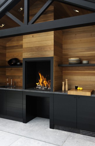 Cuisine extérieure pour un été design dans le jardin.  Conduit de cheminée et mur en teck clair, meubles de cuisine en stratifié noir ébène.