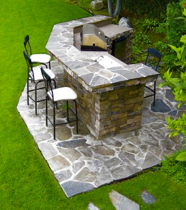 cuisine d'extérieur construite en pierre avec barbecue, évier intégrés. comptoir bar monté sur carré de sol en pierres 