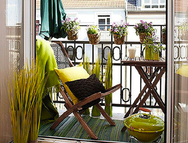 Déco petit balcon aménagé avec salon de jardin en teck et de belles nuances de vert anis avec les coussins les branchages artificiels et le barbecue de table