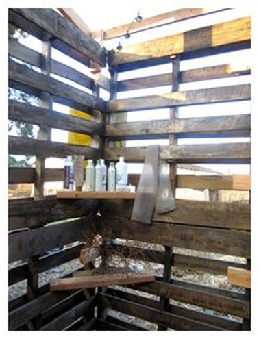 douche extérieure installée dans un mur d'enceinte construit avec des palettes bois de récup et deux petites étagères pour poser produits de douche et serviettes