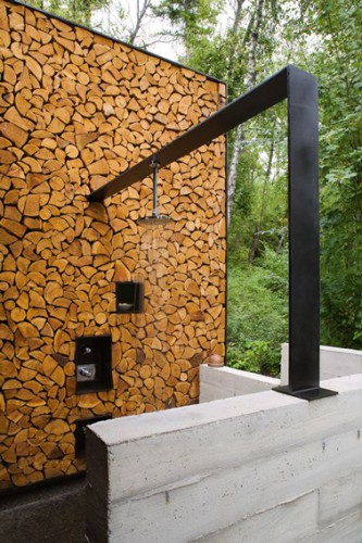 Douche de jardin installée sur poutre métallique en L qui s'appuis sur un mur monté avec des buches de bois.