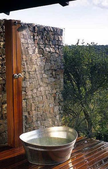 Douche extérieure en bois installée sur mur maison, en guise de receveur, une grande bassine alu posée sur sol en teck