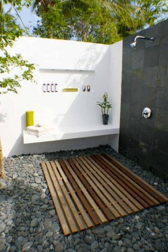 douche de jardin installée dans deux murs d'enceinte peints en blanc et gris anthracite. sur un des murs un petit banc en  béton. Au sol un caillebotis en teck