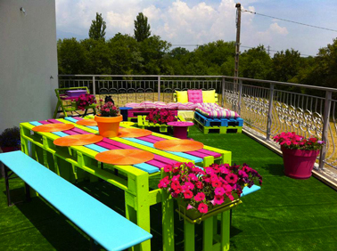Une table en palette haute en couleurs avec des palettes en bois peintes en vert anis, fushia et bleu azur. 2 palettes bois servent à construire les pieds de la table 