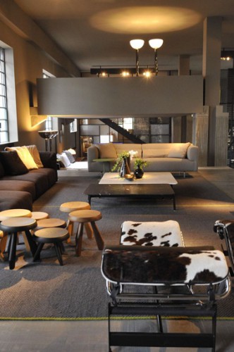 Ambiance chaleureuse dans un salon design avec la couleur taupe du sol au plafond et les deux grands canapé taupe et chocolat.. Une touche de blanc est apportée avec la chaise longue en peau de vache