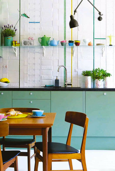 Le vert émeraude utilisé pour repeindre les meubles de cuisine est repris en écho pour le listel de la crédence est mis joliment en contraste avec le blanc du carrelage et du sol