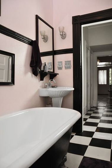 Style rétro chic pour la salle de bain rose et noir Dans une salle de bain rétro déjà équipée d'une baignoire sur pieds, c'est la peinture des murs rose pale soulignée de bande de peinture noire qui complète le style. Pour rester dans l'harmonie, miroir et linge de toilette noir