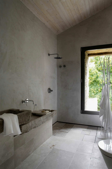 Authenticité d'une déco minimaliste pour une ambiance zen dans cette salle de bain aux murs en béton et carrelage au sol gris réchauffés par le lambris bois du plafond en pente