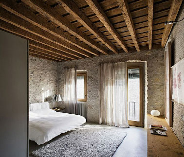 Dans un appartement moderne, belle réalisation pour une chambre zen avec des murs de pierres et briques blondes. Profitant d'une situation au dernière étage, le plafond est mis a brut pour profiter de l'aspect chaleureux des poutres apparentes et du plancher 