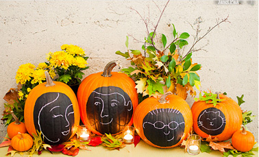 Décoration de citrouilles d'Halloween avec des dessins de visages de la famille faits à la craie et intégrées dans une composition de branchages, feuilles rouge et bougies
