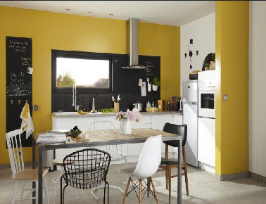 Conviviale et bien aménagée une cuisine blanche boostée par une peinture couleur jaune sur le mur du linéaire plan de travail  qui offre à la pièce un sérieux gain de luminosité. Originale, le cadre de fenêtre élargi peint en noir pour faire office de crédence. Une idée à retenir pour une cuisine moderne. 