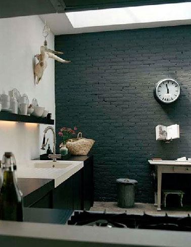 Dans la cuisine d'une maison de campagne le mur de brique peint en noir avec les autres murs blanc confère à la pièce un esprit design renforcé par les lignes épurés du plan de travail noir et blanc