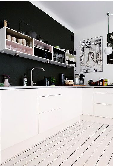 Dans cette cuisine blanche le mur de la crédence peint en noir s'anime du damier formé par les meubles hauts sans portes où certains fonds ont été retirés 