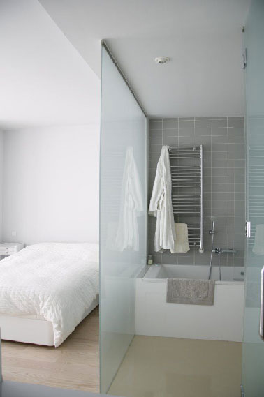 Une paroi de verre sablé pour séparer la salle de bain installée dans une chambre d'adulte. Cette séparation de pièce permet à la salle de bain de bénéficier de la lumière naturelle apportée par la fenêtre