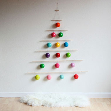 Un sapin bien rigolo assemblé avec des boules de couleurs crochées sur des bois flottés puis fixé au mur, une idée astucieuse et déco pour gagner de la place.