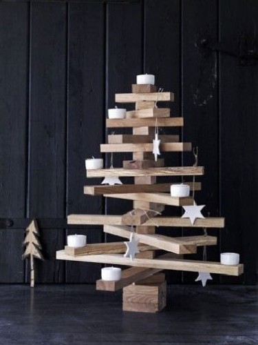 Design, un sapin de Noël style accumulation Kapla Un sapin en bois au design épuré réalisé avec des planches de bois assemblées tels une construction de kapla et décoré de bougies et étoiles blanches