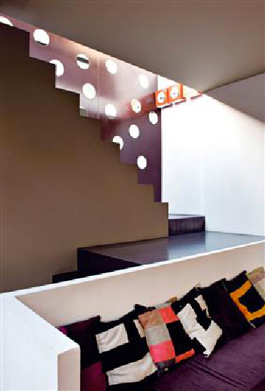 Jeu de Couleurs Aubergine et Gris Pour Structurer un Salon Moderne Dans ce salon ouvert sur l'escalier, le mélange de aubergine, gris et terre doré appliqués sur les murs délimite chacune des zones. L'intensité des couleurs est renforcée par le muret blanc qui accueille la banquette réalisée sur mesure où l'on retrouve la couleur aubergine pour le tissu des coussins d'assise.
