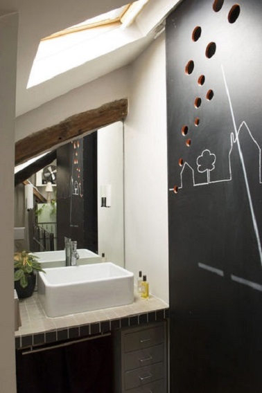 Une petite salle de bain mansardée avec un miroir pour agrandir l'espace Dans cette petite salle de bain, la cloison ardoise dissimule les WC et la douche à l'italienne. Une colonne de rangements prend place sous la vasque et un miroir coupé aux mesures agrandit l’espace