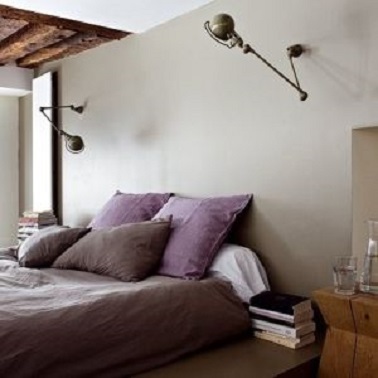 La couleur taupe du mur de cette chambre est relevée par la teinte parme des draps.  L'ensemble donne une chambre à la déco très tendance et une ambiance sereine.