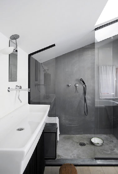 Une douche installée sous pente dans la tendance de la salle de bain grise. Lumineuse avec le velux qui la surplombe,  le béton ciré  gris recouvre murs et sol  de la douche à l’italienne pour mieux en délimiter l'espace. Les deux parois de verre assurent la transparence sans empiéter sur l'espace de cette petite salle de bain