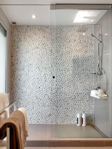 Ambiance cocooning pour une douche à l'italienne aux murs en petits galets et carrelage gris. Pour compléter cette dominante minérale, le sol de la douche est fait en béton ciré couleur terre naturelle traité anti-glisse
